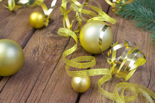 Christmas composition of yellow Christmas balls, fir branches, and a gold ribbon on a brown wooden background