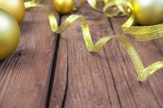 Christmas composition of yellow Christmas balls, fir branches, and a gold ribbon on a brown wooden background