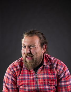 Funny guy with long hair and beard, wearing plaid shirt winking with eye in studio