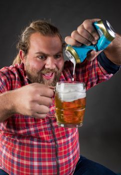 Young funny man pouring beer from can to mug against black background