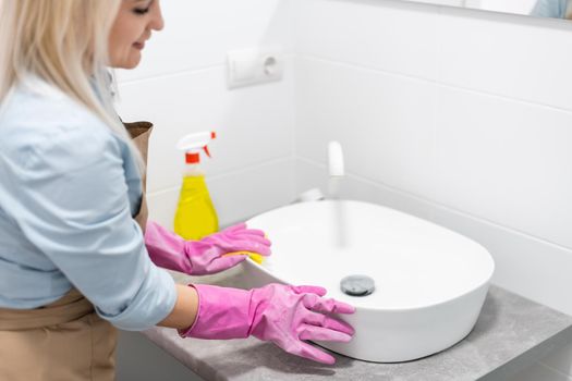 Housework and domestic lifestyle: woman doing chores in bathroom at home, cleaning wash basin and tap with spray detergent