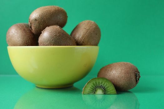 still life kiwi fruit in a yellow bowl plate and next to a kiwi copyspace slice.