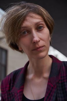 young woman with short hair in red checkered jacket outdoors in front of building. portrait of caucasian female
