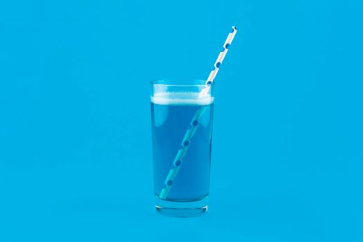 Blue lemonade with gas bubbles and a cocktail straw isolated on blue background. Blue Cocktail Drink monochrome banner with copy space.