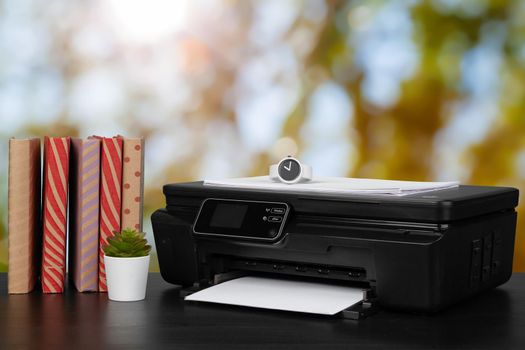 Stack of books and home printer against blurred background, close up