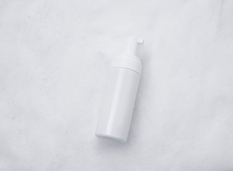 White plastic tube mockup with moisturizer cream, shampoo or facial cleanser and gentle soap foam with bubbles on marble background, top view. Treatment spa beauty skincare cosmetic product.