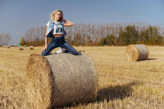 Beautiful girl villager posing in jeans on a bale of hay in a field