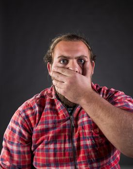 Man holding hand over mouth to stop saying something and is being shocked, shoot in studio