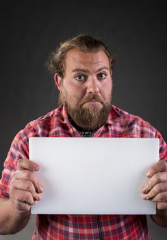 Man, worker in plaid shirt with beard and long hair with funny face expression holding small horizontal blank white board, in studio