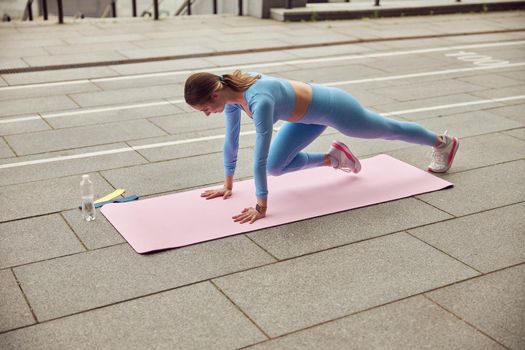 Beautiful fit caucasian woman is doing exercises outdoors at the city