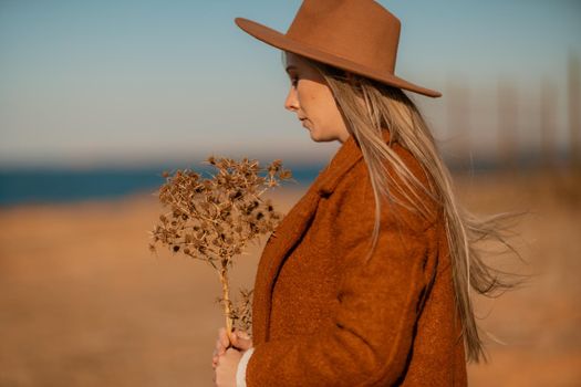 A woman walking along the coast near the sea. An elegant lady in a brown coat and a hat with fashionable makeup walks on the seashore.