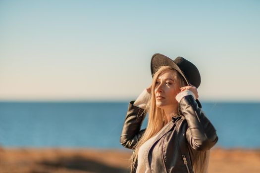 A blonde in a stylish black leather jacket walks along the seashore