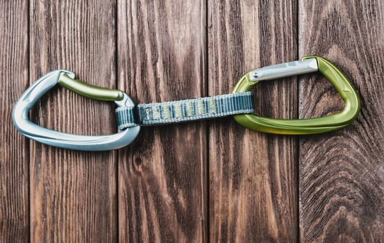 One quickdraw for climbing sport on a wooden background, close-up.