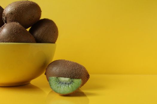 Still life of fruit trending illuminatiited yellow kiwi in a bowl plate of yellow and next pieces of kiwi yellow background copyspace.