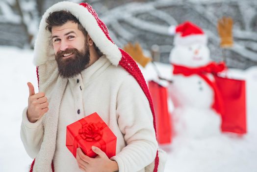 Winter man. Snowman and funny bearded man with gift. Happy father with Christmas gift over winter snowman background