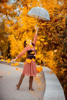 Beautiful girl in a dress with an umbrella in the autumn park. She holds him over her head, autumn leaves are falling out of him.