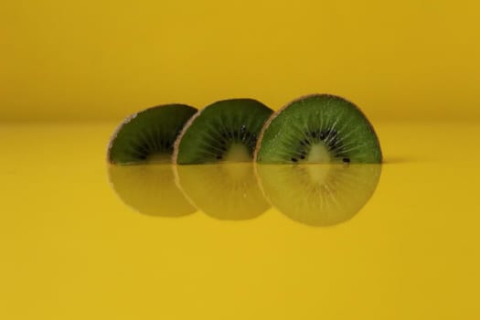 Three slices of kiwi halves lie in a row on trend iluminaited yellow with a copy of the space place for text.