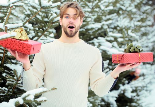 Excited amazed man holding Christmas gift in snow wood outdoor. Merry Christmas and happy new year. Macho with presents on winter day.
