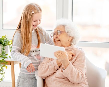 Happy granny with granddaughter using tablet at home