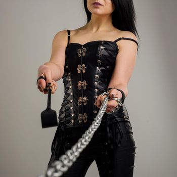 Sensual woman in black leather corset with chain and riding crop in hand - image