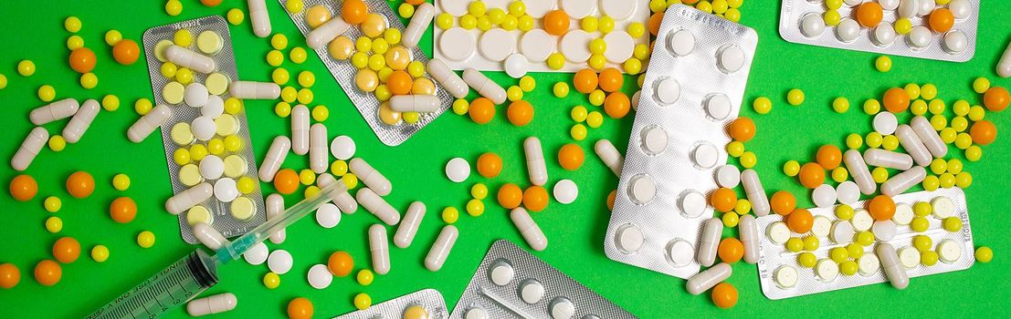 colorful and white pills, capsules, syringe. Prevention, cure of influenza, coronavirus, covid-19. yellow, orange vitamins, tablets on green background. medical healthcare, protection concept banner