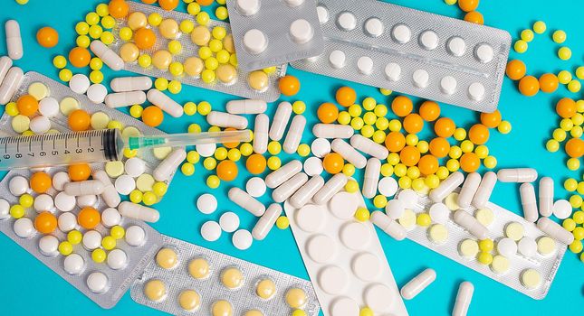 colorful and white pills, capsules, syringe. Prevention, cure of influenza, coronavirus, covid-19. yellow, orange vitamins, tablets on blue background. medical healthcare, protection concept banner