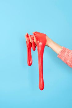 Close up on shiny Red or coral slime in the hand isolated on blue background. Fun and stress relief concept