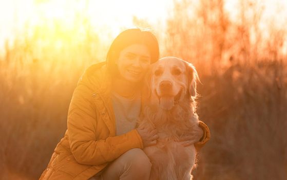 Girl hugging golden retriever dog with sunset light outdoors. Young woman petting doggy pet labrador at nature at autumn