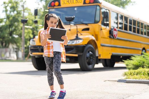 adorable little schoolgirl near school bus and looking at camera