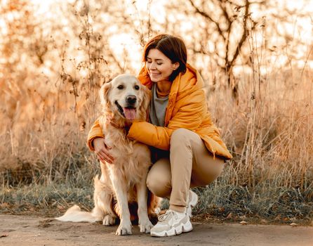 Girl hugging golden retriever dog with sunset light outdoors. Young woman petting doggy pet labrador at nature at autumn
