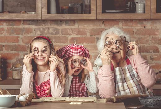 Happy granny with granddaughters smiling and looking at camera through cookie cutters