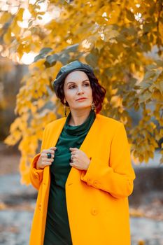 Beautiful woman walks outdoors in autumn. She is wearing a yellow coat and a green dress. Young woman enjoying the autumn weather. Autumn content