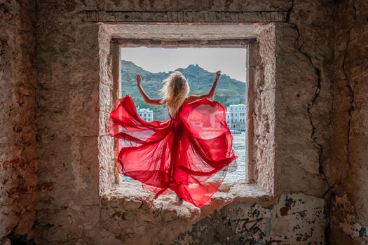 View of Balaklava Bay through an arched balcony in oriental style. The girl in a long red dress stands with her back. Abandoned mansion on the Black Sea coast.