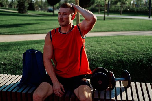 Cheerful male athlete in the park sits on a bench. High quality photo