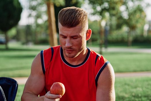 man in the park sits on a bench and eats an apple summer. High quality photo