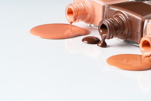 Nude colors nail polish spilled over white background. Close up.