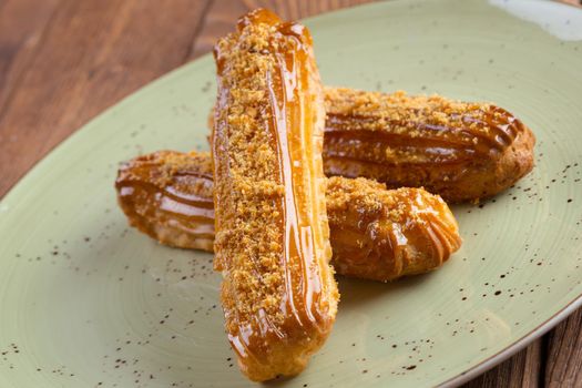 Three eclaies with nuts topping on green plate close up