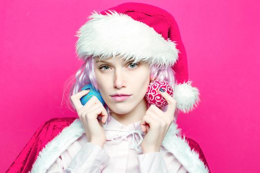 Young woman or cute girl in christmas santa hat holds Christmas balls on pink background. Closeup face portrait.