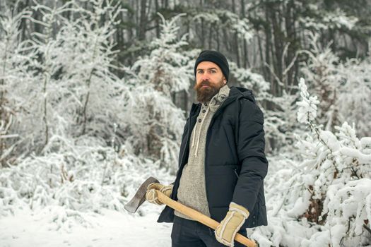 Man lumberjack with axe outdoor in winter. Bearded man with axe in snowy forest