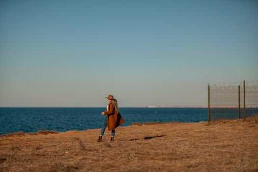 A woman walking along the coast near the sea. An elegant lady in a brown coat and a hat with fashionable makeup walks on the seashore.