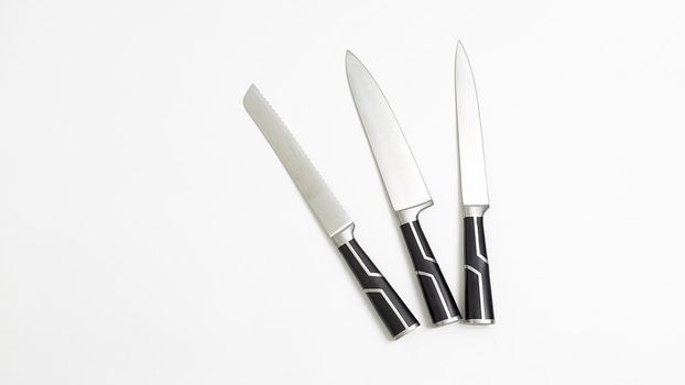 three sharp kitchen knives with black handles isolated on white background. top view on group of knives with shining metal blades. simple flat lay composition with copyspace. Space for text