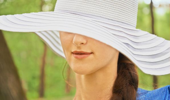 Mysterious woman in hat with wide brim in park in the summer