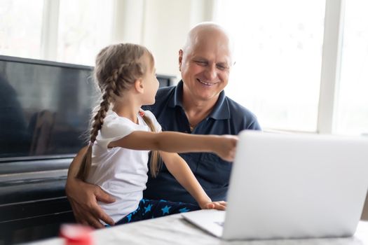 Grandfather and his granddaughter using a laptop together.