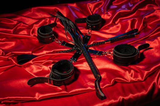 Top view of bdsm outfit. Bondage and whip crossed spank on the red linen. Adult sex games. Kinky lifestyle. - image