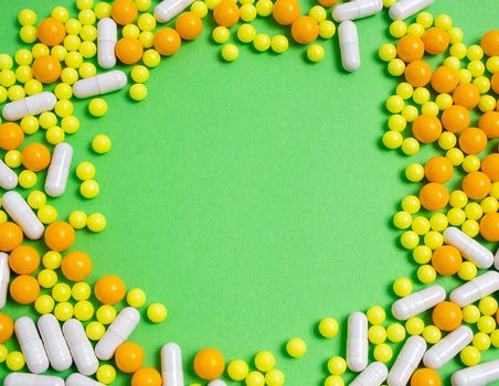 colorful pills for viral diseases in circle frame with copyspace for text. Prevention of influenza, coronavirus, covid-19. yellow, orange vitamins on green background. medical healthcare concept