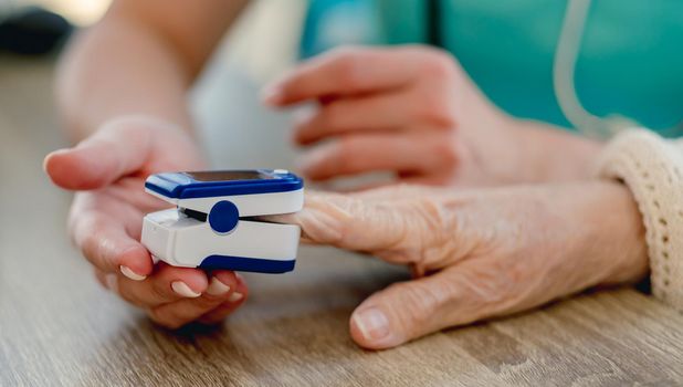 Doctor using pulse oximeter on old woman hand during appointment in clinic