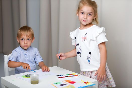 The boy and girl, brother and sister paint watercolors at the table on white sheets of paper. Concept aesthetic development of children, happy childhood.