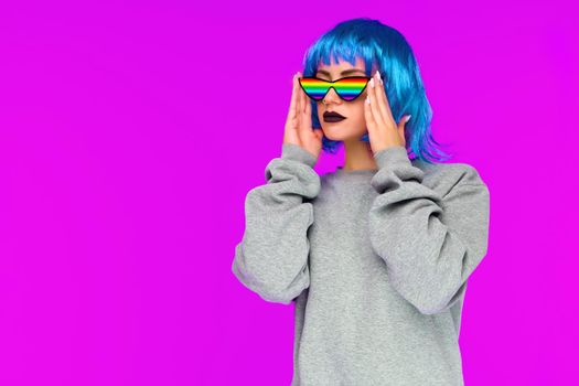 Lesbian girl in blue wig and rainbow sunglasses looks to the side on pink background - image