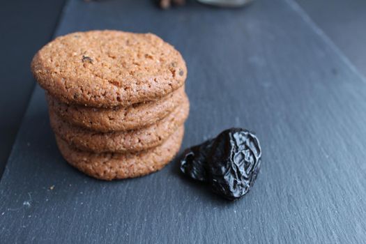 Eating still life cookie oatmeal homemade with prunes and cinnamon sticks lies a stack of slides on a black background with room for text copyspace.