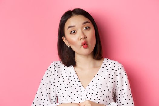 Beauty and lifestyle concept. Close-up of funny and cute asian woman pucker lips, showing fish mouth and standing playful, standing over pink background.